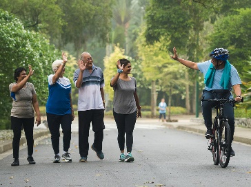 A person riding a bike waving to a group of people walking together in a park.