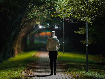 A person walking through a public park at night with bright lights along the path.