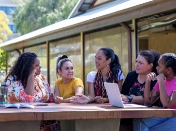 A group of Aboriginal people having a conversation at a bench outside.