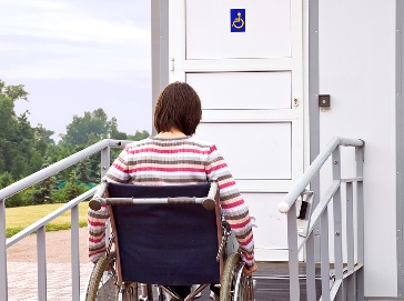A person with a mobility aid using an accessible ramp to access a toilet in a public space.