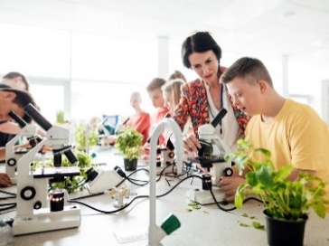 A group of people in a classroom using microscopes with a teacher supporting them.