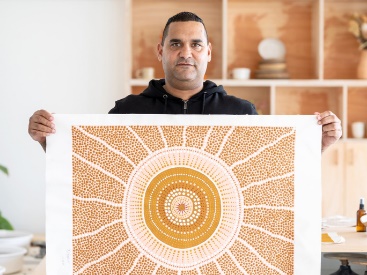An Aboriginal person holding a painting.