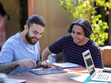 2 people working together writing in books and using a digital tablet.