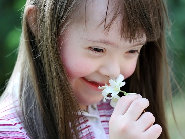 A person smelling a flower in a park.